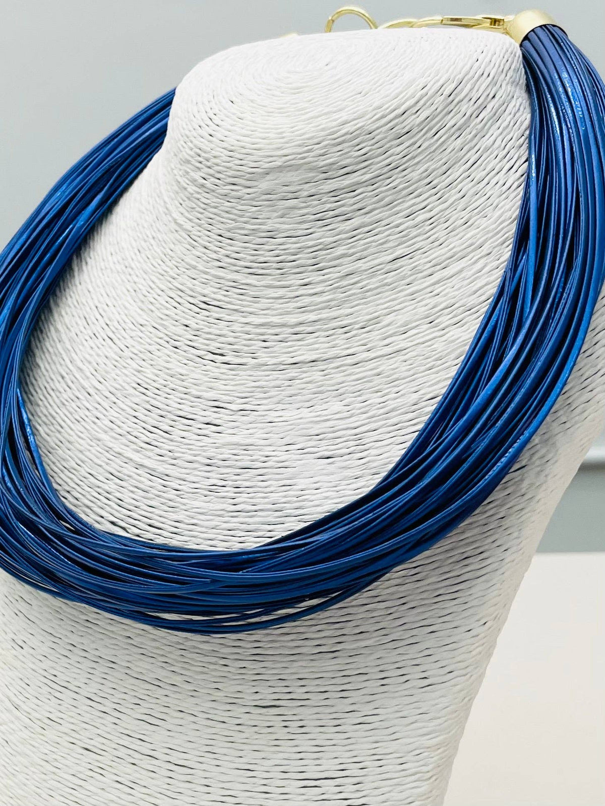 Blue necklace on a mannequin head with a gray background