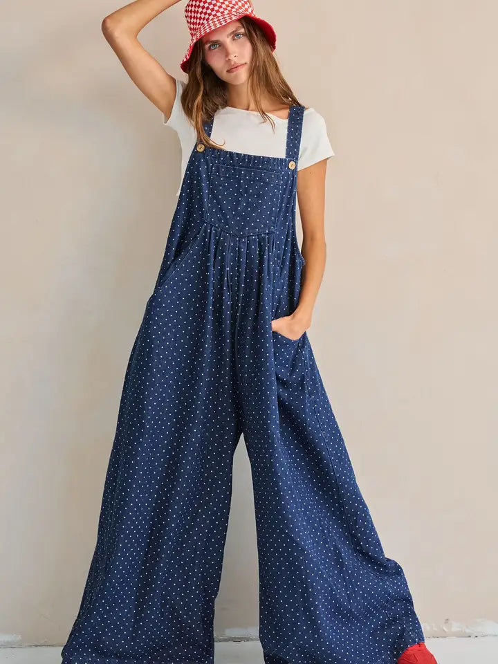 Navy polka dot wide-leg overall jumpsuit, close-up front view with hand near strap buttons