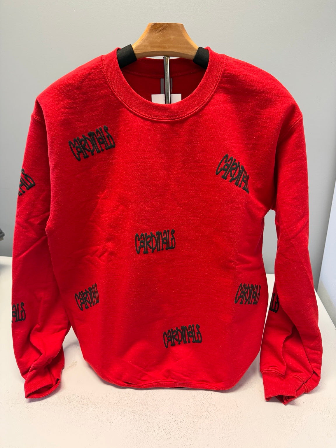 A bright red long-sleeve crewneck sweatshirt with black 'Carnalith' text printed all over, displayed on a wooden hanger against a light gray background.