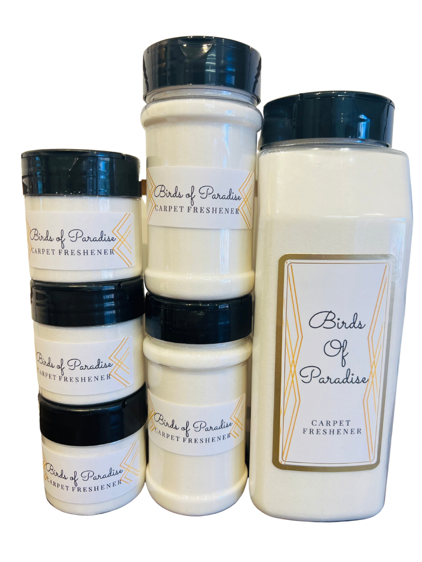 Three bottles of Birds of Paradise luxury carpet freshener in different sizes with white labels and black caps, displayed on a wooden surface with foliage in the background.