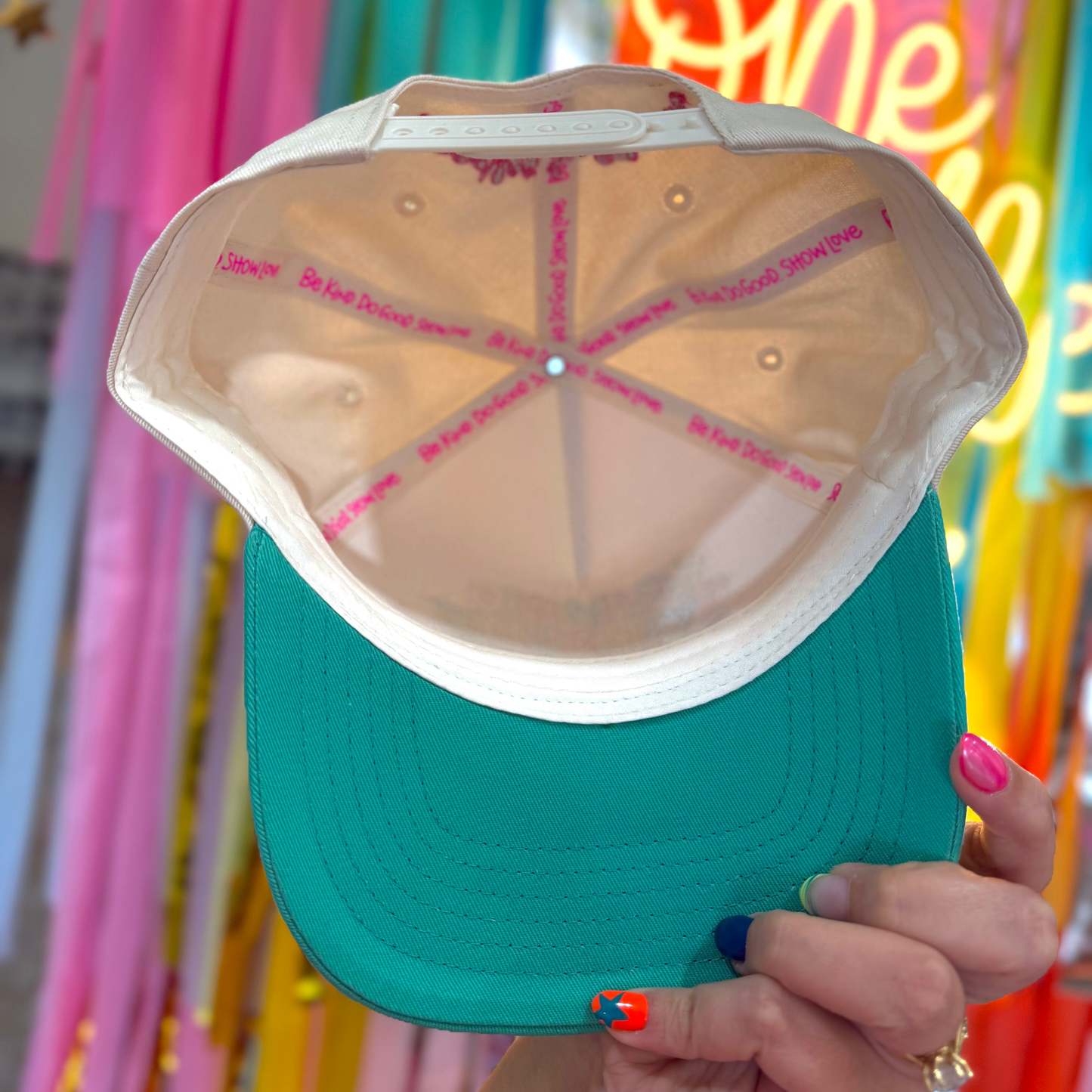 Teal cap with white interior being held in front of colorful background