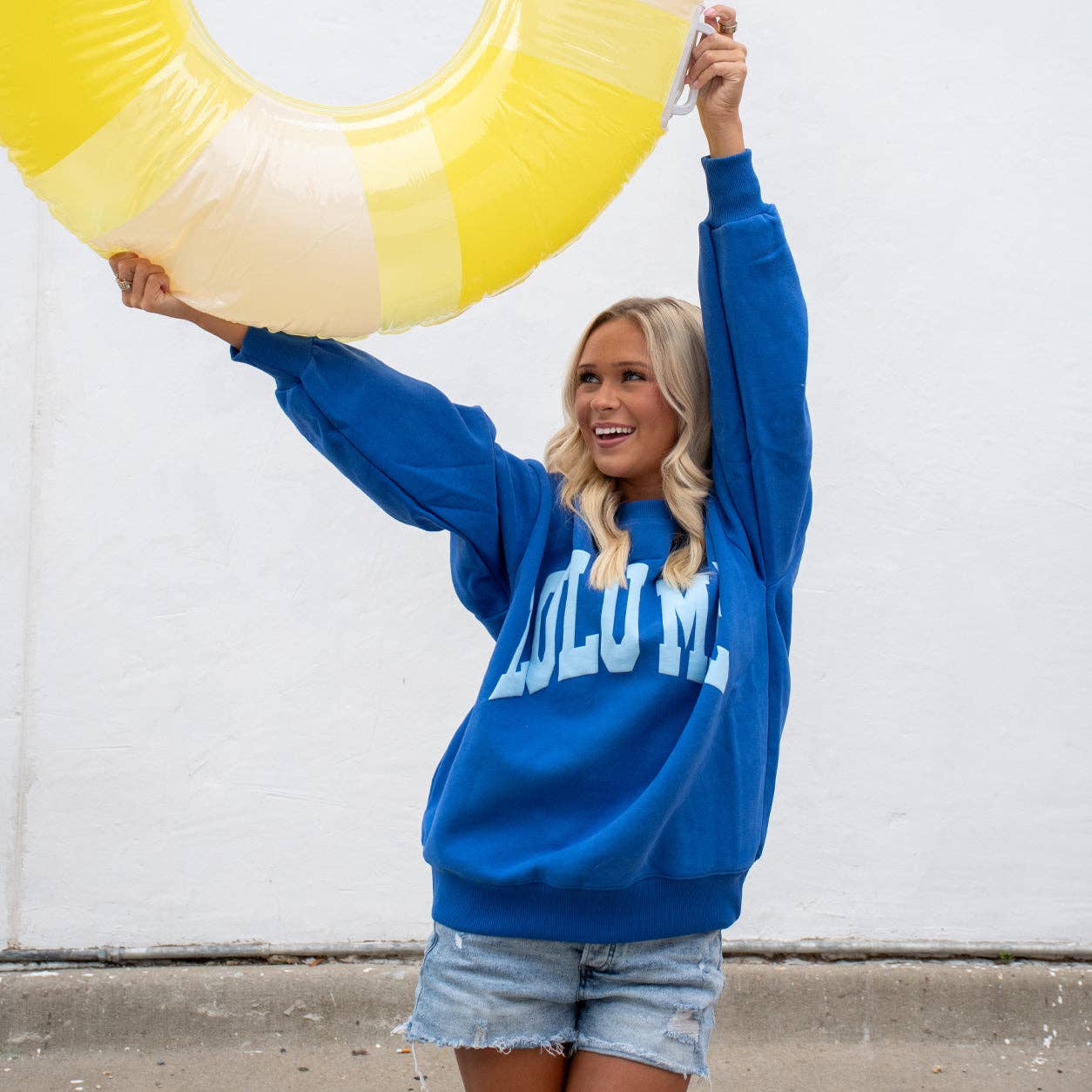 Woman wearing Lulu Mac Royal Blue Puff Sweatshirt with light blue raised lettering and denim shorts.