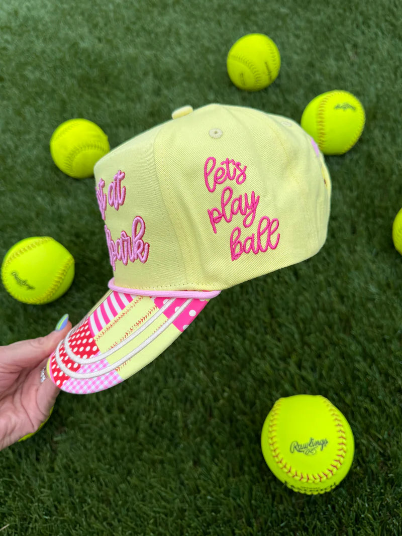 Yellow cap with 'let's play ball' text on a grass background with tennis balls.