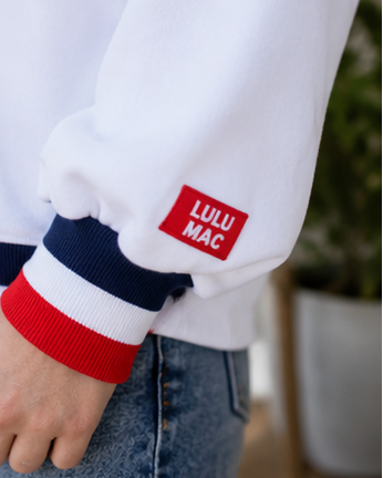 Woman wearing a white sweatshirt with 'LULU MAC' text, sitting on a couch, and standing outdoors.