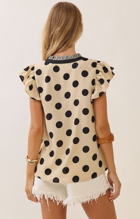 Woman wearing a polka dot blouse with ruffled sleeves on a plain background