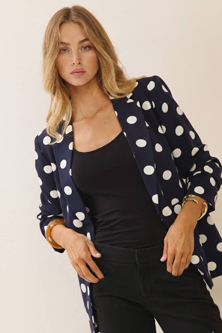 Woman wearing an Oddi navy and white polka dot blazer featuring ruched sleeves and a classic collared silhouette.
