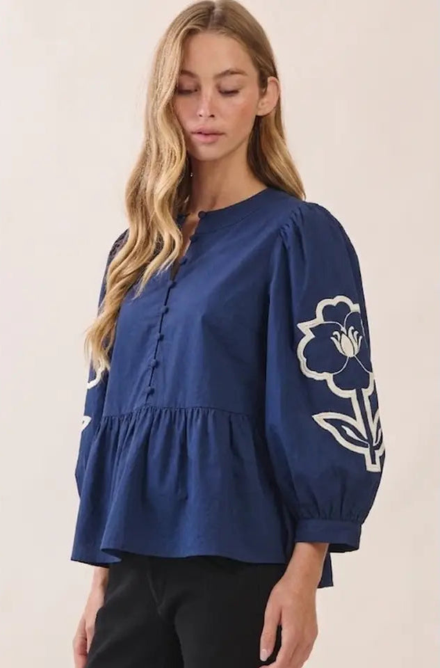 a navy floral embroidered button up top modeled with black pants