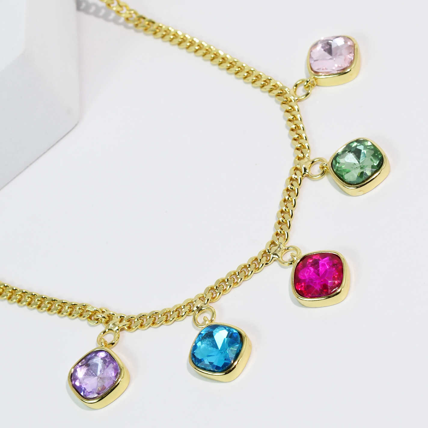 Gold chain necklace with colorful gemstone pendants on a white background by treasure jewels