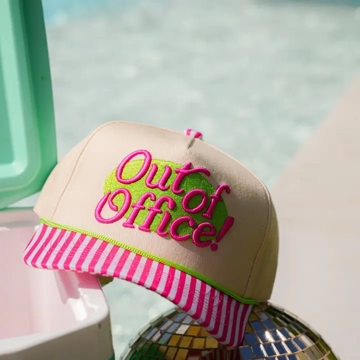Beige cap with pink and green 'Out of Office!' text on a blurred background