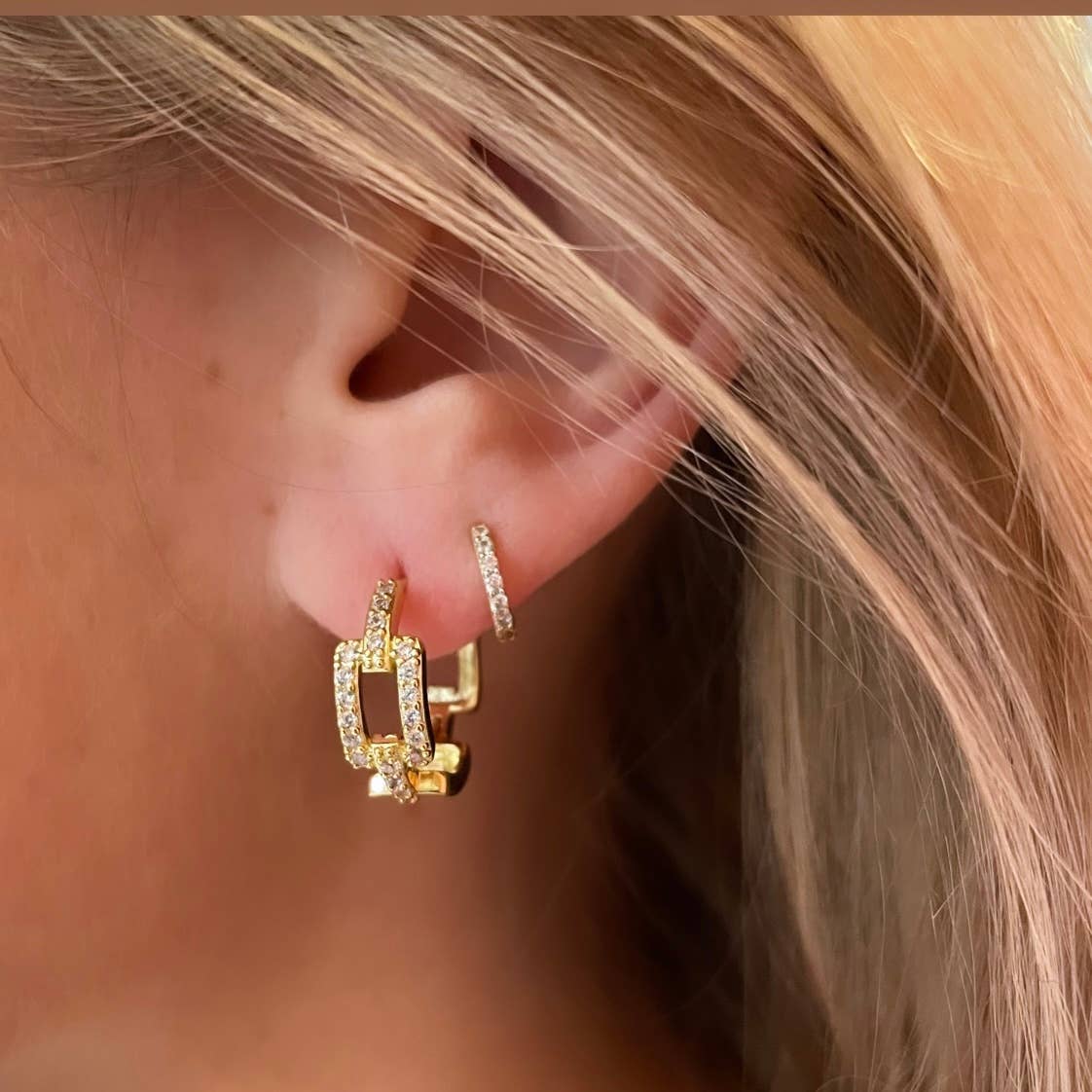 Close-up of an ear wearing gold hoop earrings with a blurred background