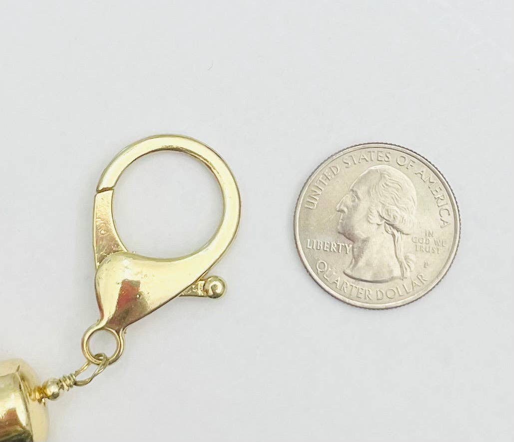 Gold lobster clasp next to a quarter on a white background