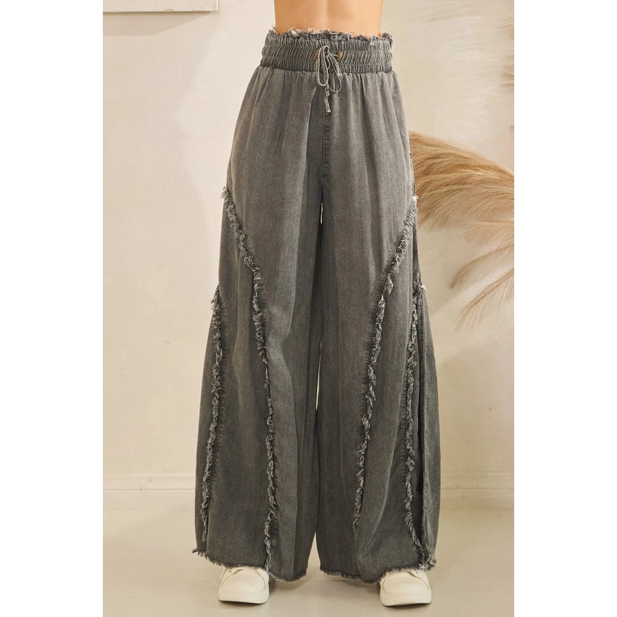 A person wearing wide-leg gray pants with frayed trim and an elastic drawstring waist, shown from the waist down against a light indoor wall.