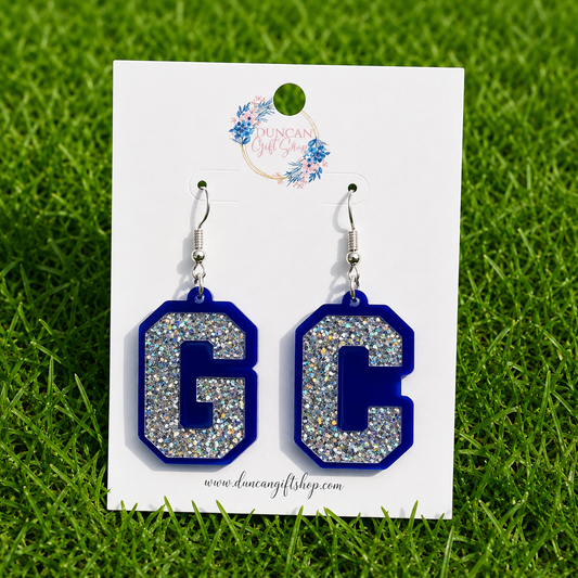 A pair of letter C drop earrings with silver glitter centers and royal blue borders, displayed on a white card with the brand logo 'Dancing Gift Shop' against a green grass background.