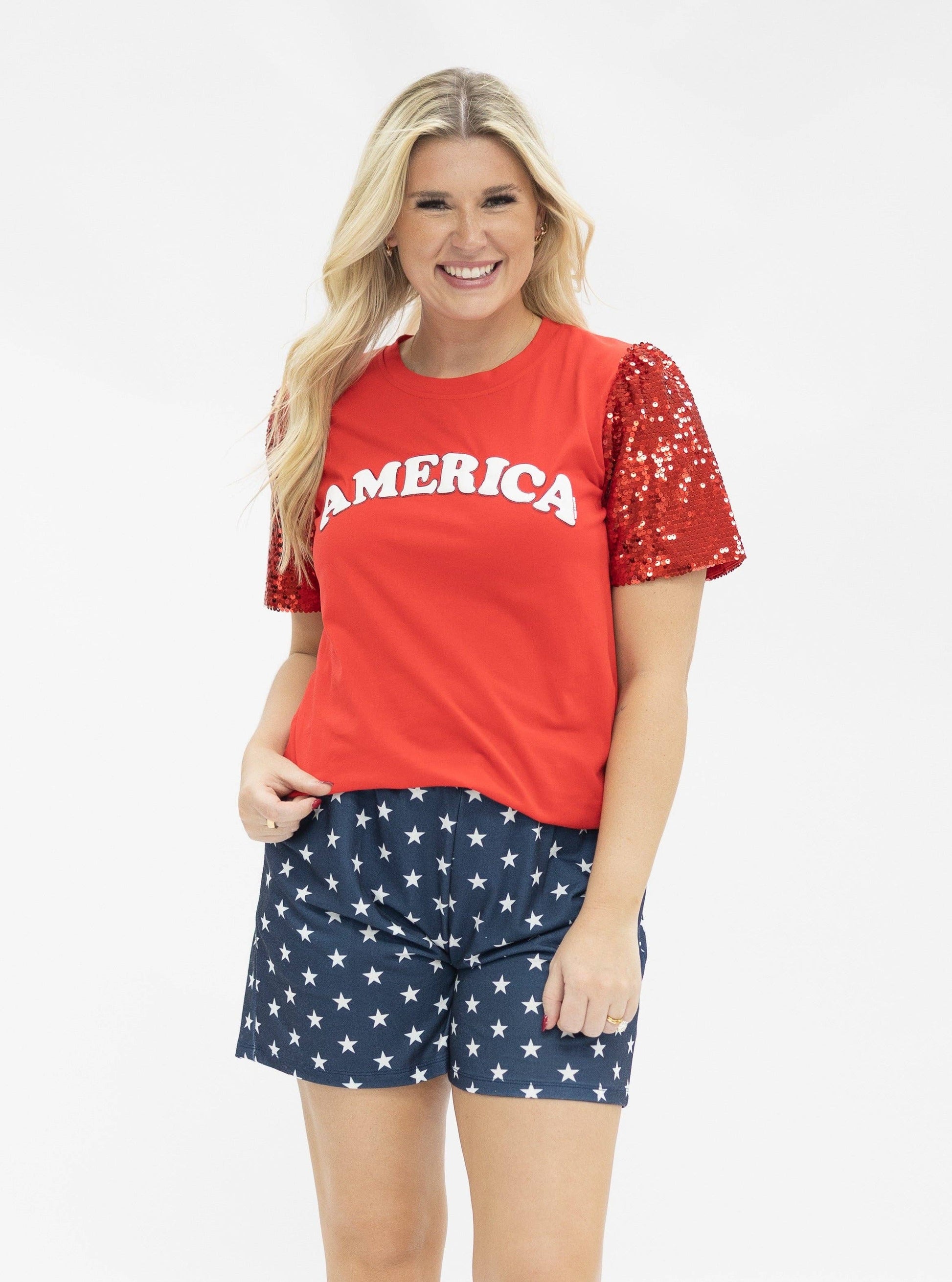 Woman wearing a red 'AMERICA' t-shirt with sequin sleeves and star-patterned shorts on a white background