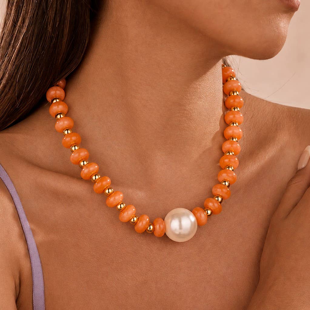 An orange beaded necklace with small gold spacer beads and a large white pearl pendant, shown worn on a model's neck.