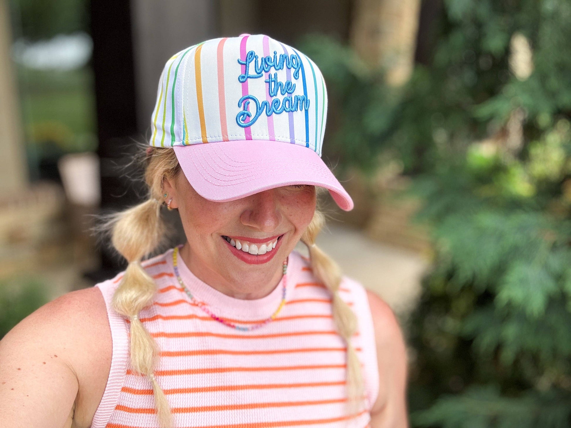 Person wearing a colorful striped cap with text and a pink top outdoors.