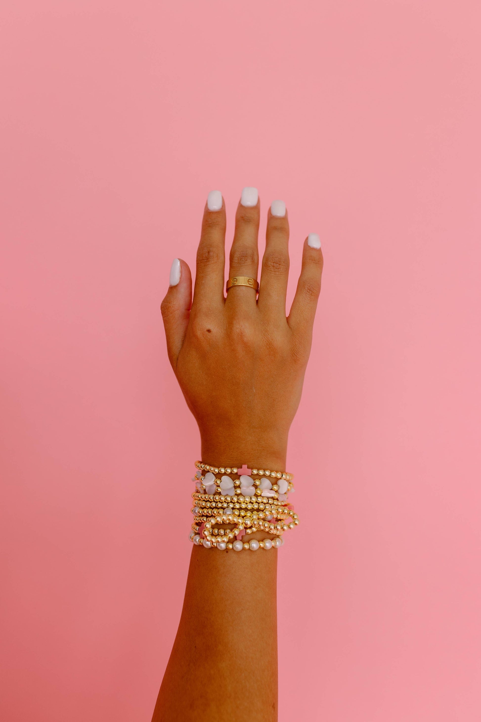 Hand wearing gold bracelets on a pink background