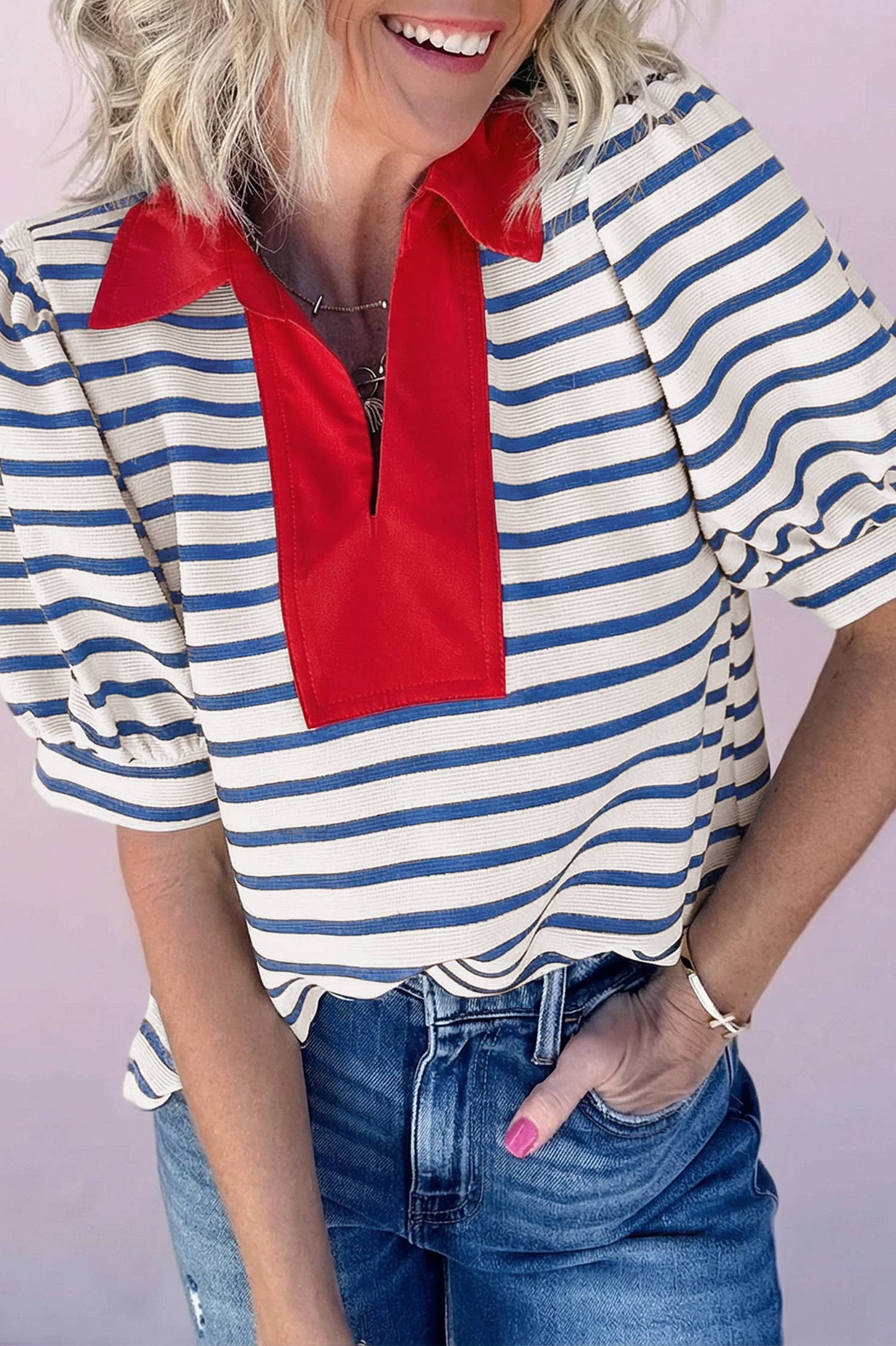 Woman wearing blue and white striped V-neck top with bold red contrast collar and denim jeans