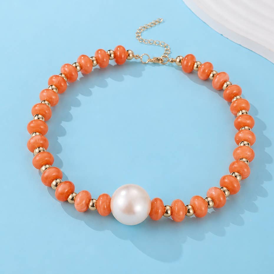 A coral orange beaded necklace with small gold spacer beads and a large white pearl at the center, displayed on a light blue background.