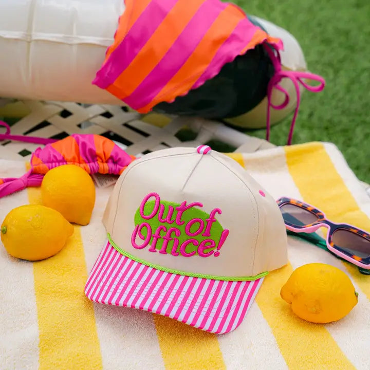 Beige cap with pink and green 'Out of Office!' text on a towel with lemons and sunglasses.