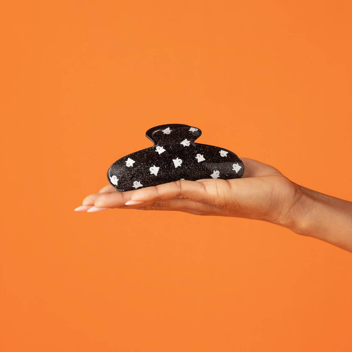 A hand holds a black glittery hair claw clip decorated with white star patterns against a solid orange background.