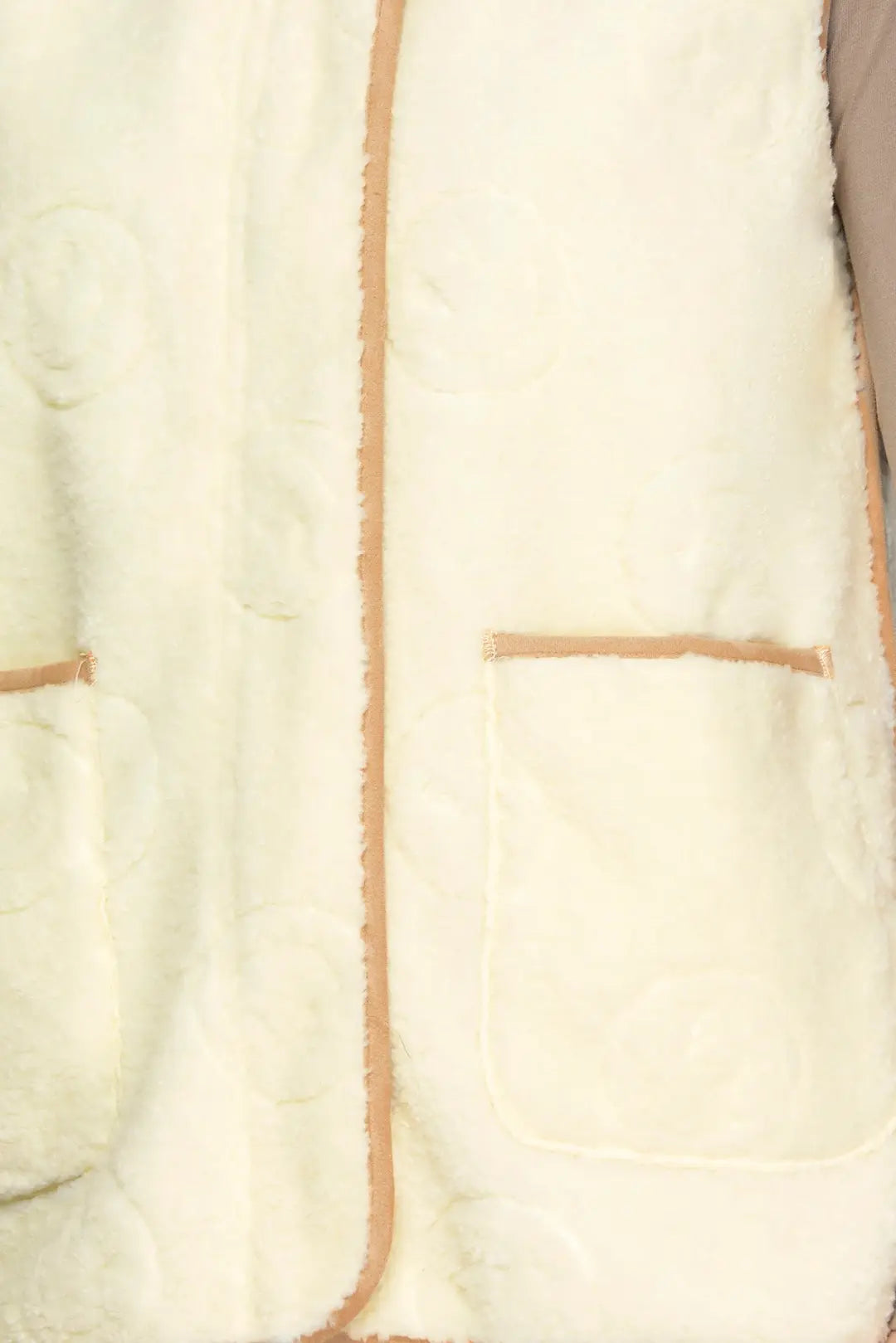 Close-up of a cream-colored plush fleece jacket or vest with tan contrast stitching and a quilted circular pattern.