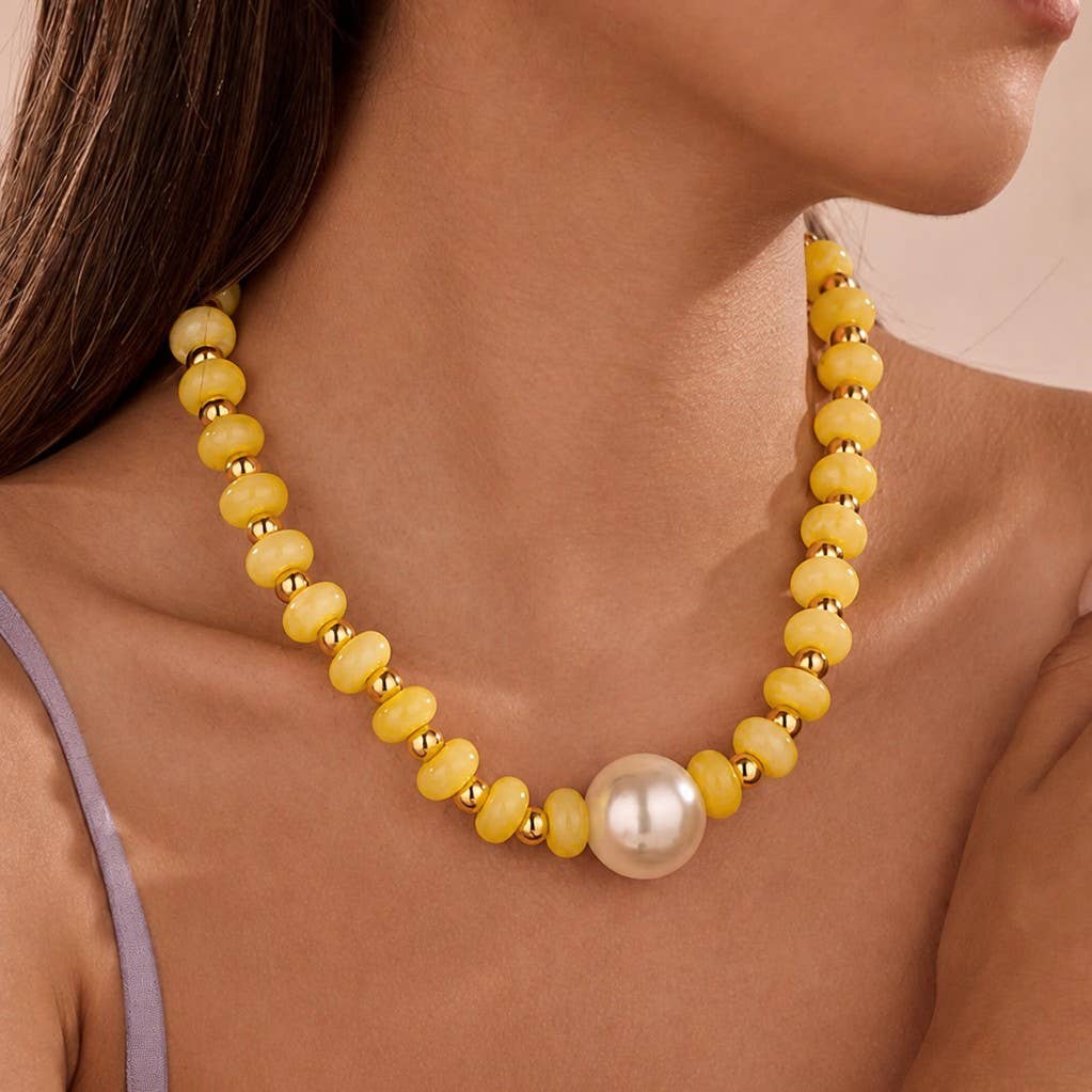 A close-up of a model wearing a yellow beaded necklace with small gold spacer beads and a large white pearl at the center.