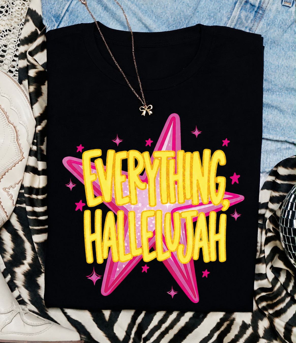 Black t-shirt with 'Everything Hallelujah' text in yellow and pink on a patterned surface.
