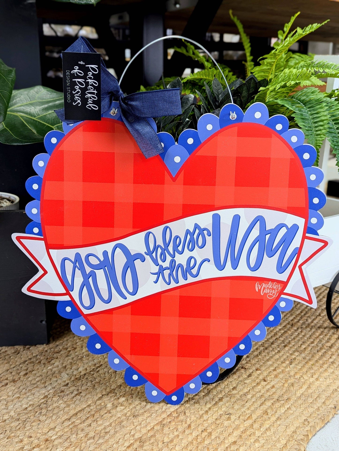 Heart-shaped sign with red checkered pattern and blue text, featuring a blue bow on top, on a textured surface.