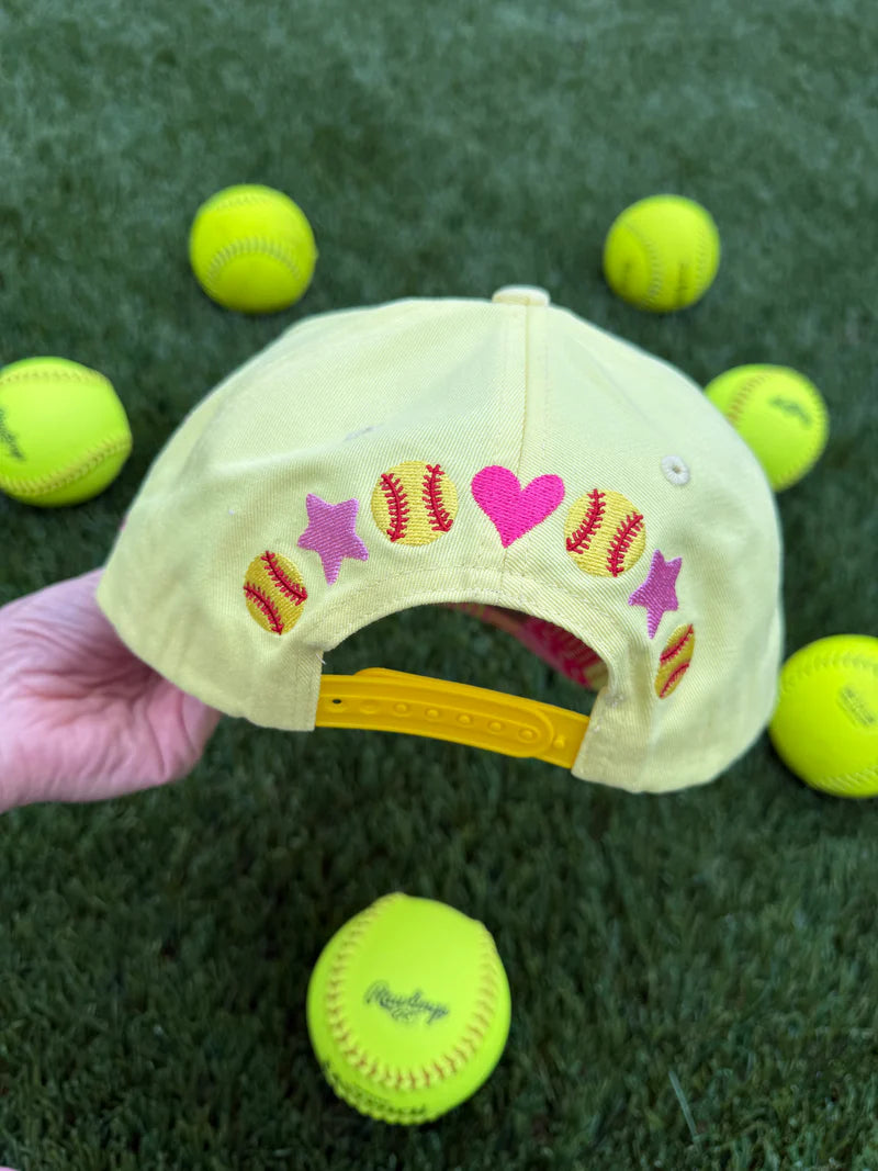 Yellow cap with heart and star designs held over green tennis balls on grass
