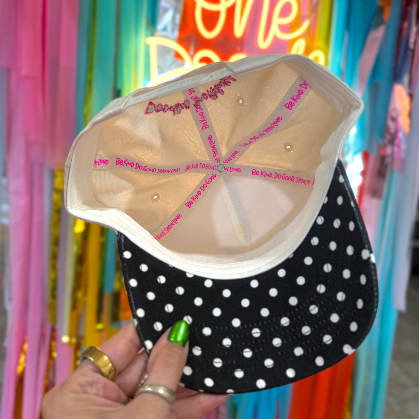 Black and white polka dot cap held by a hand with colorful background