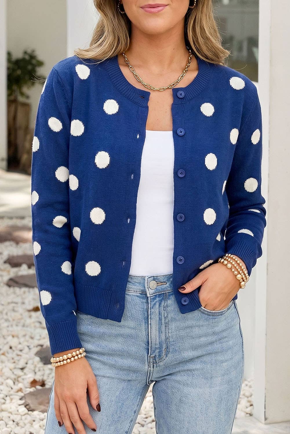 Woman wearing a blue polka dot cardigan with a white top and jeans outdoors.