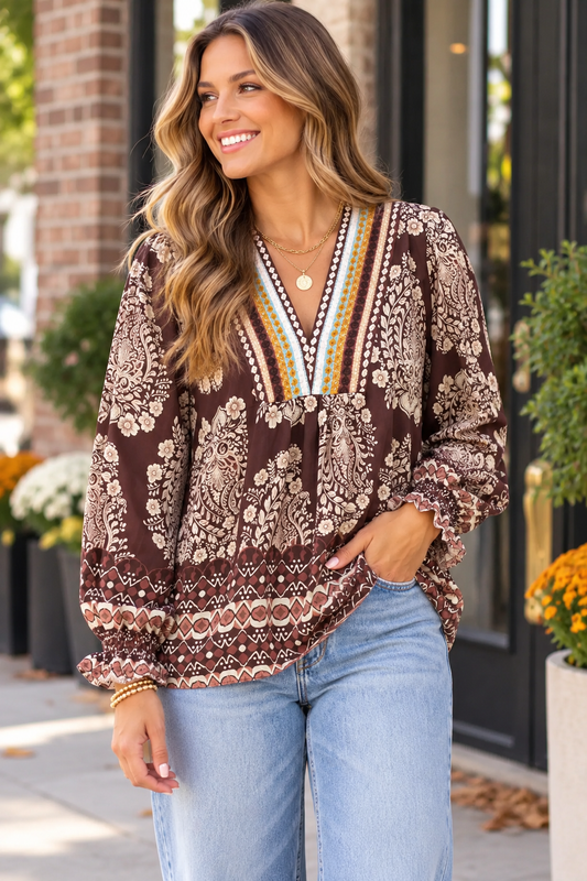 A woman wearing a brown bohemian patterned blouse with a V-neck and light blue jeans, standing outdoors in front of a brick building.