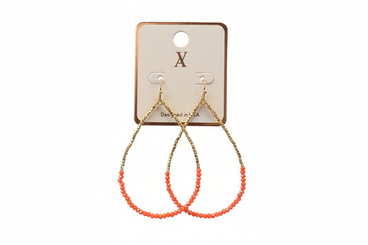 earrings with orange beads and gold chain held over a jewelry box in an indoor setting.