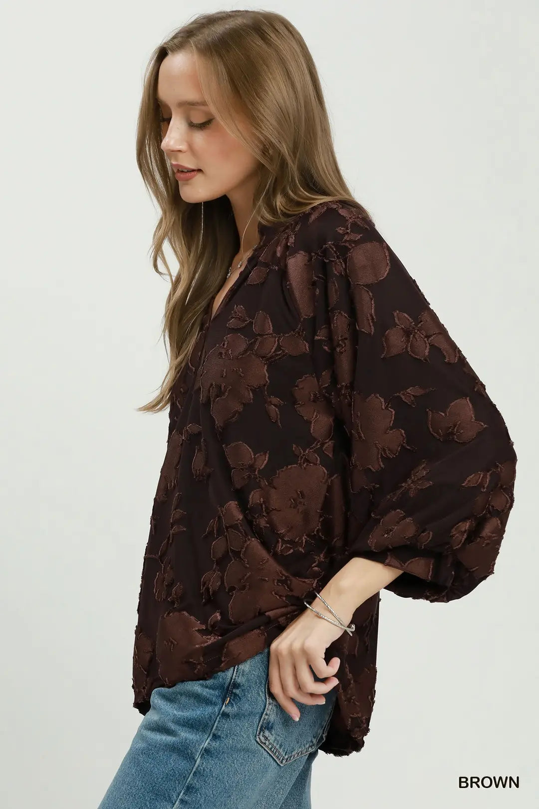 Woman wearing a brown floral blouse with blue jeans on a white background