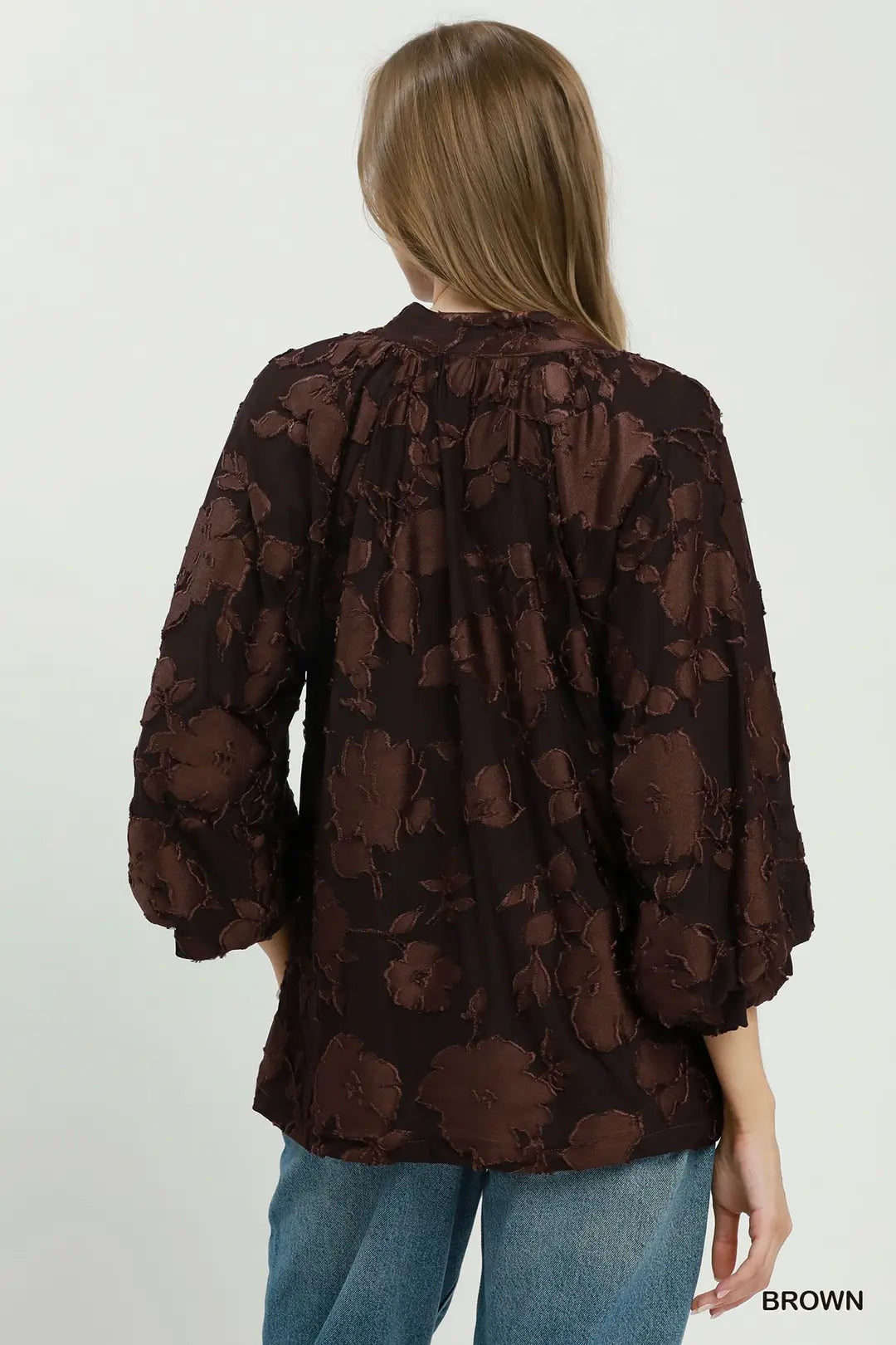 Woman wearing a brown floral blouse with blue jeans on a white background