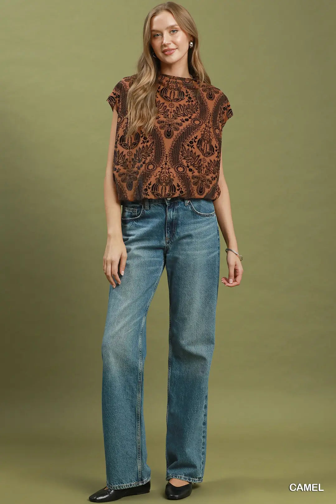 Woman wearing a patterned top and blue jeans against a green background