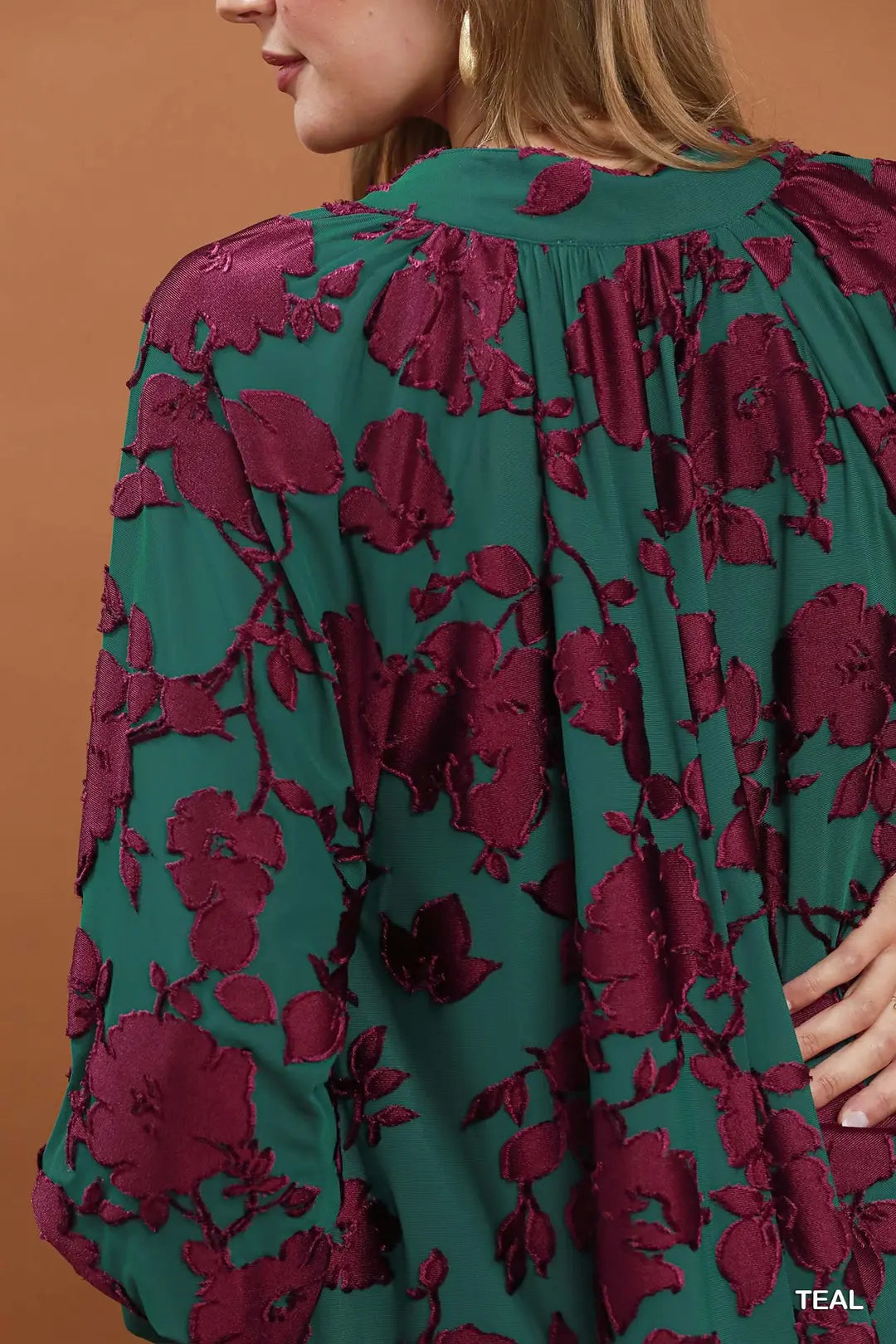 Green and red floral patterned garment on a person against a brown background