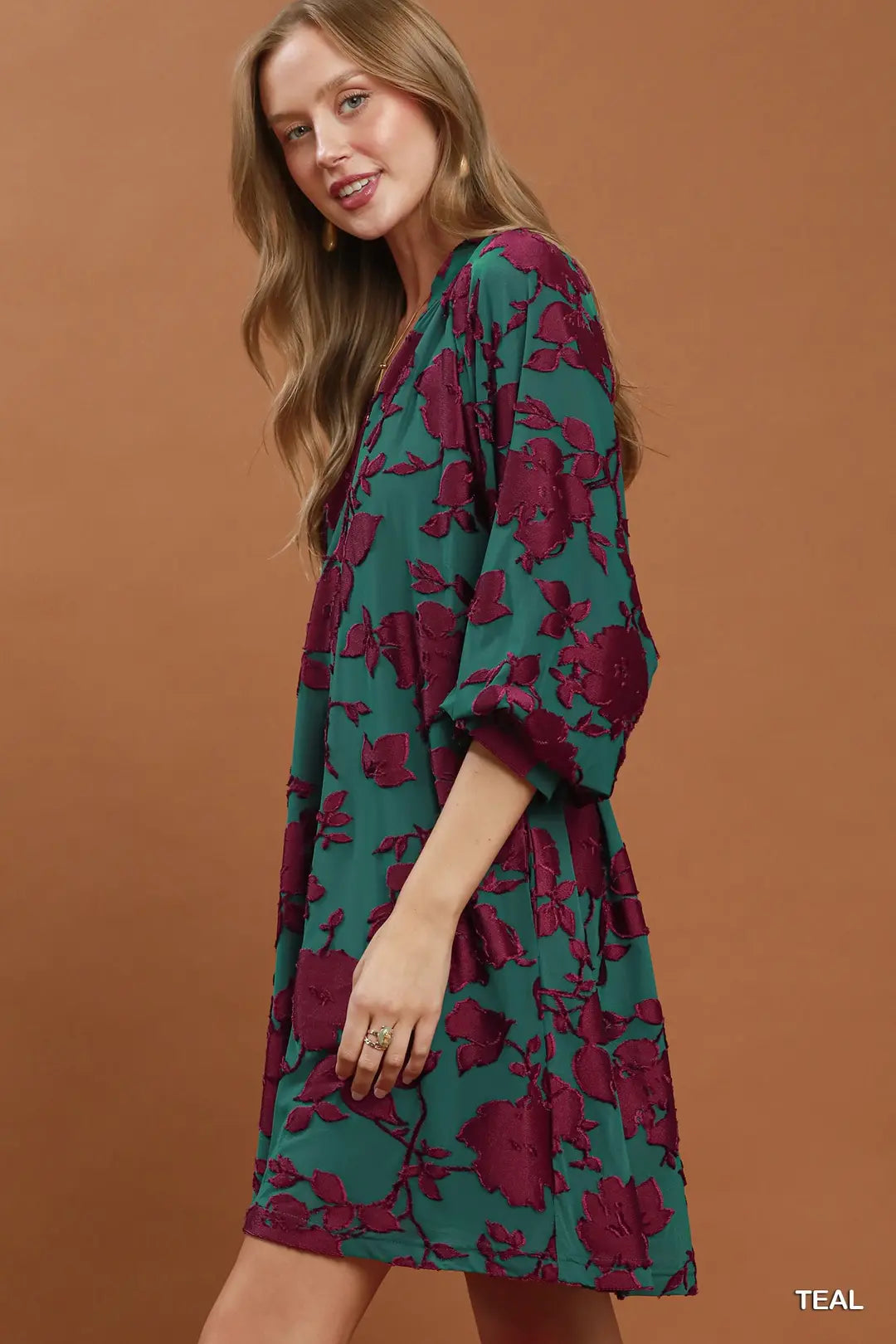 Woman wearing a teal and purple floral dress against a brown background
