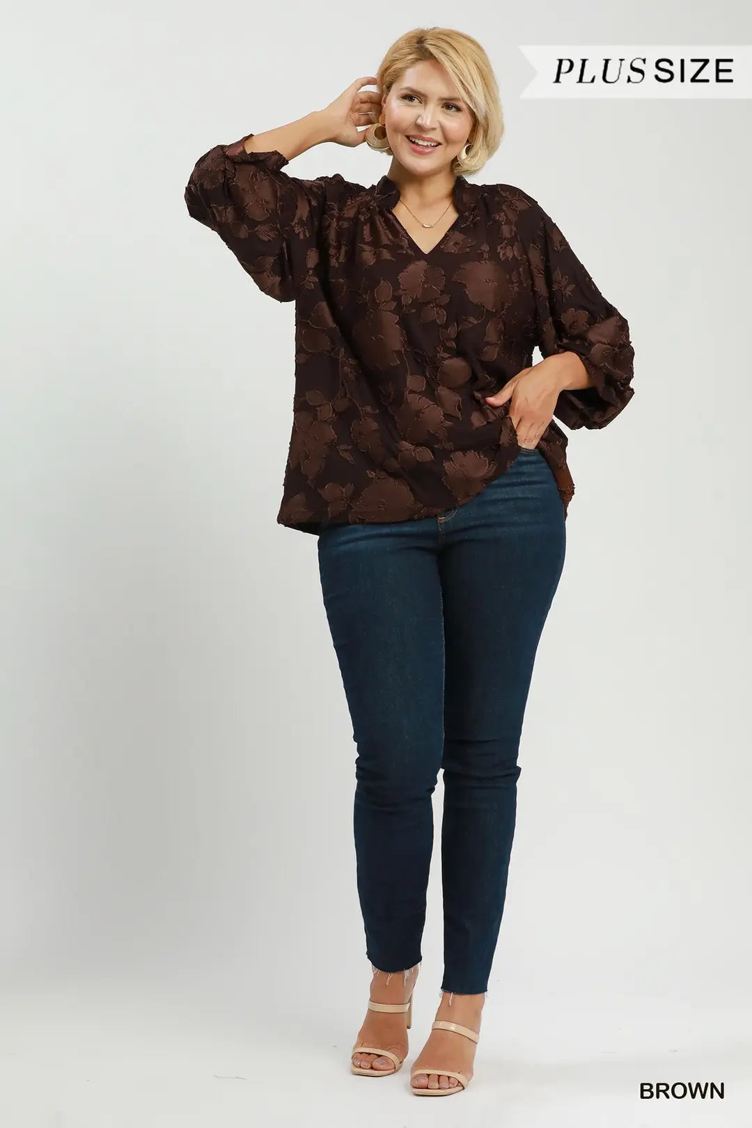 Woman wearing a brown patterned blouse and blue jeans on a white background