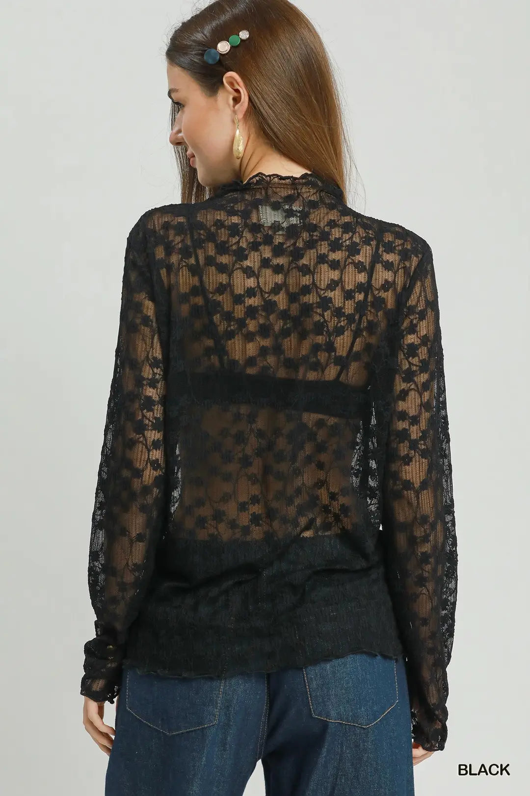Woman wearing a black sheer lace top with long sleeves on a plain background