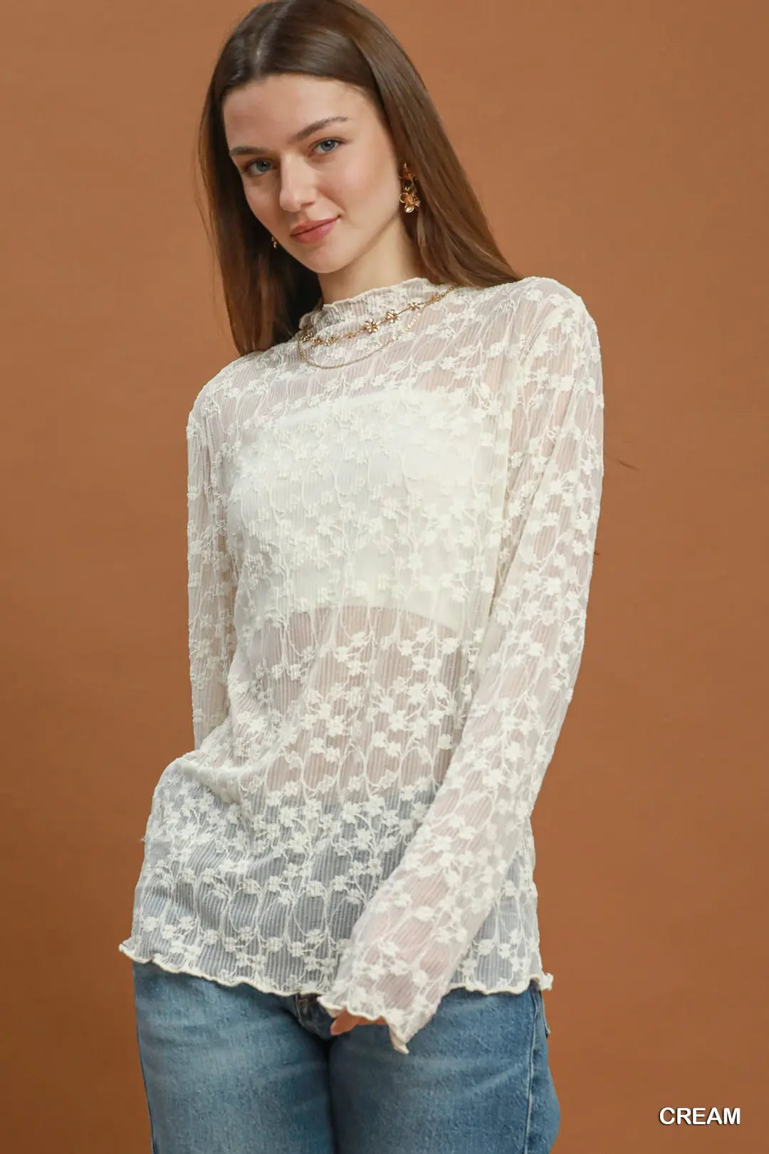 Woman wearing a cream lace top with long sleeves against a brown background