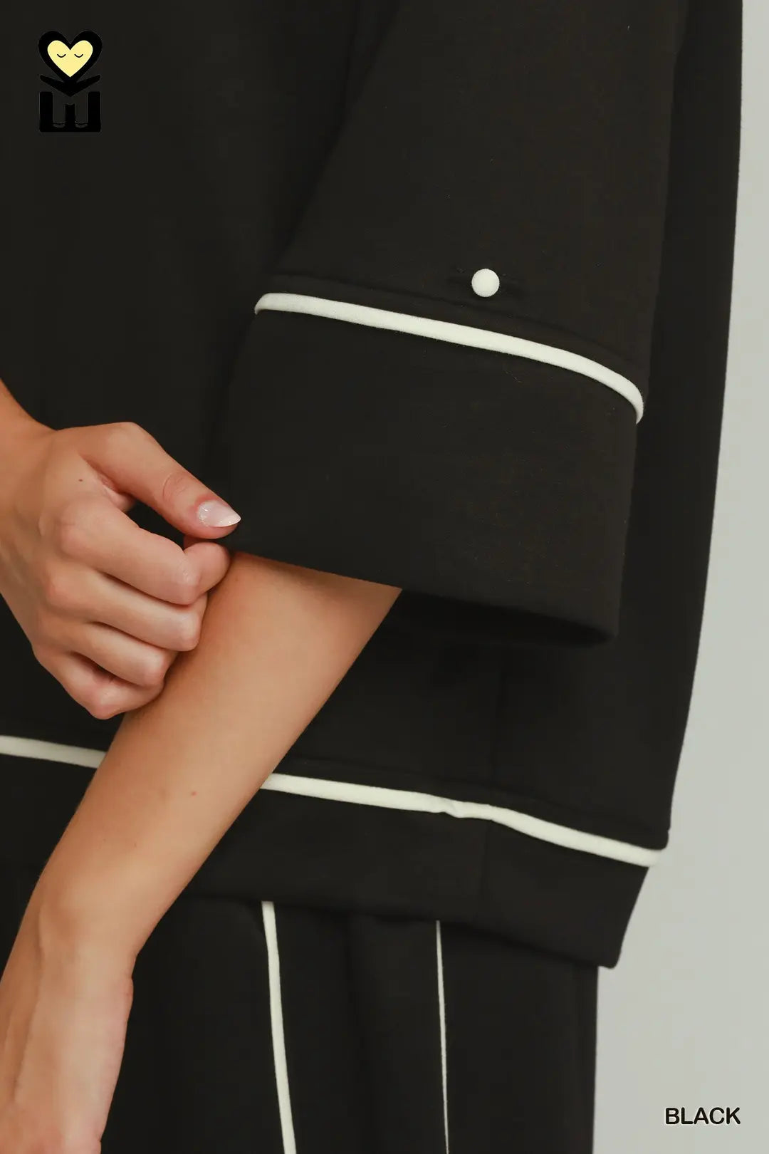 Close-up of a person wearing a black outfit with white piping trim on the sleeve and hem, showing the hand and arm. The word BLACK is printed in the bottom right corner.