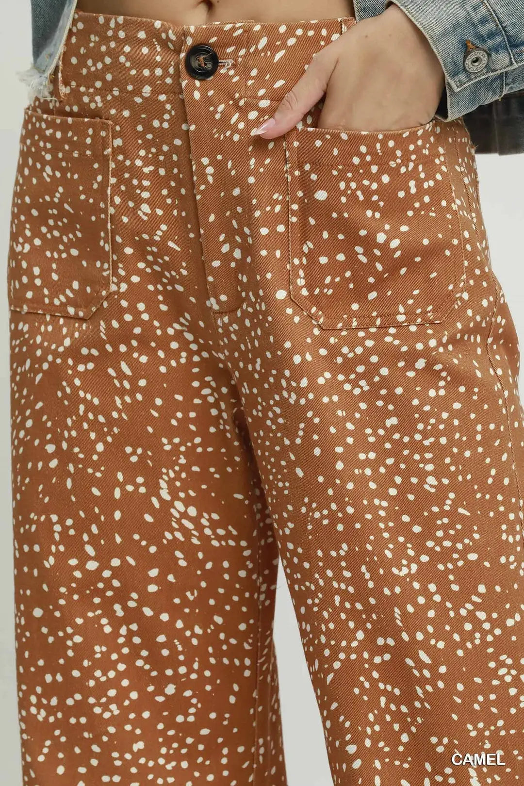 Close-up of a person wearing camel brown pants with a white speckled animal print, featuring side pockets and a denim jacket hem visible at the waist.
