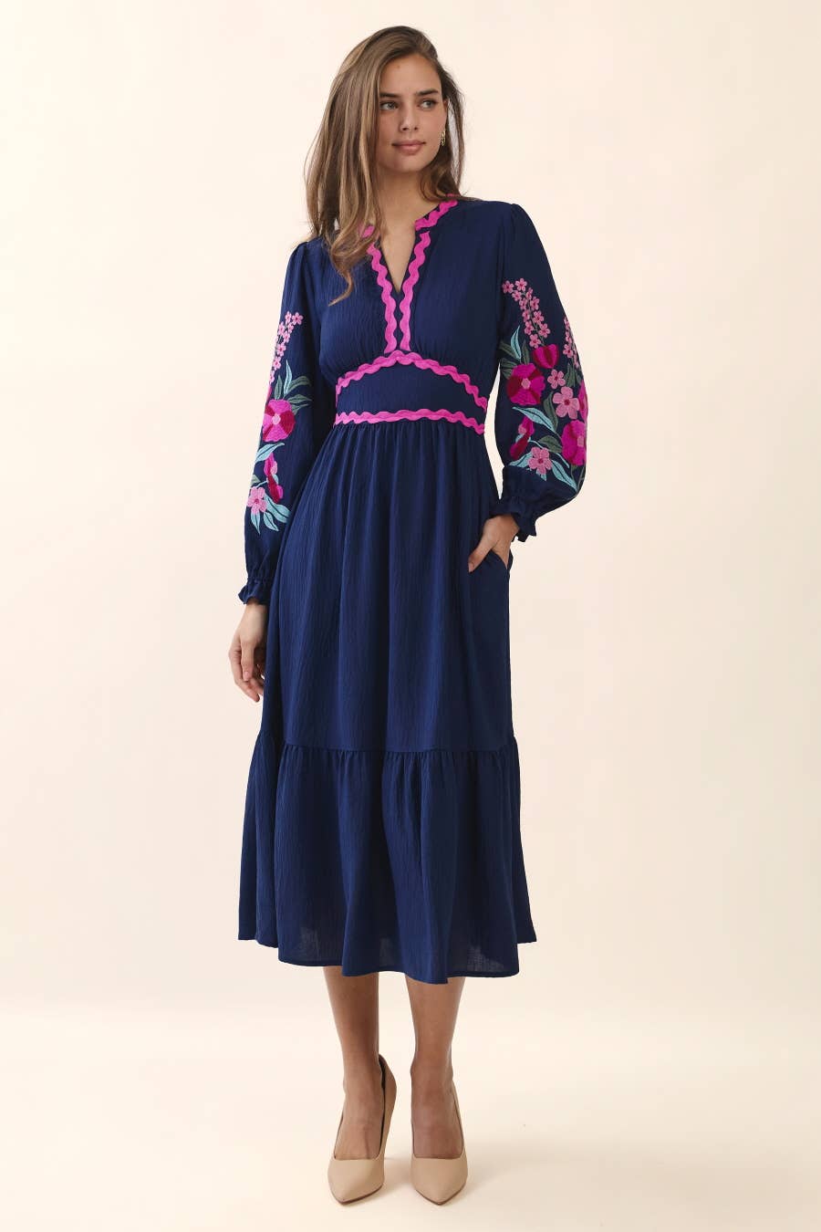 Woman wearing a navy dress with floral embroidery on a beige background