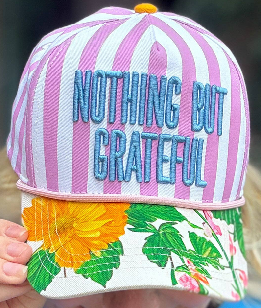 Person holding a colorful cap with 'Nothing But Grateful' text against a blurred green background