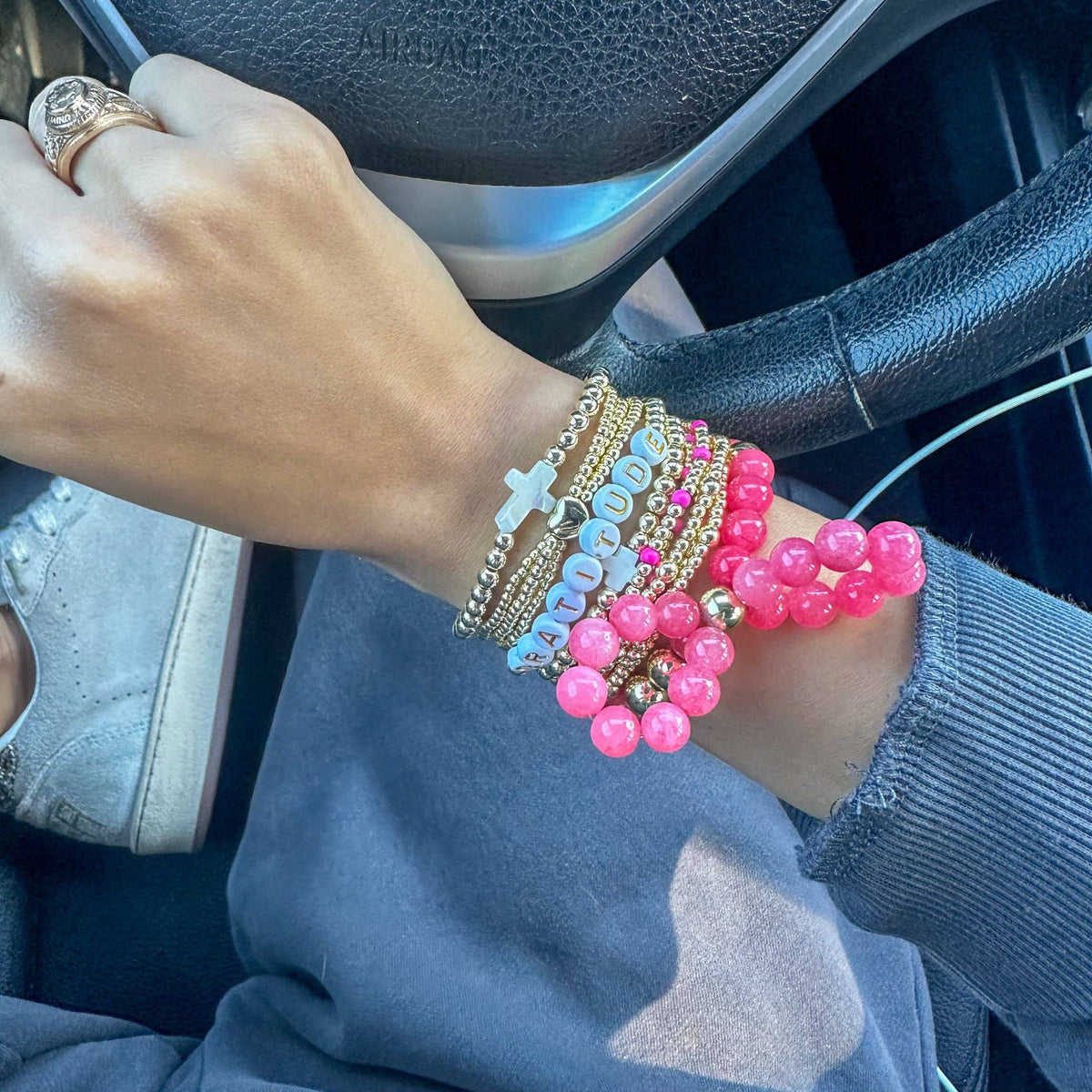 Person's wrist with multiple bracelets, including pink beads, in a car.
