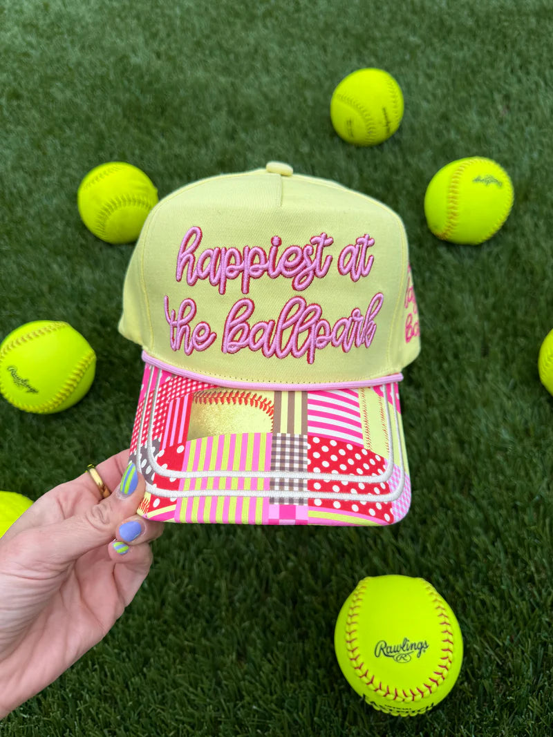 Yellow cap with pink text on a grass background with tennis balls