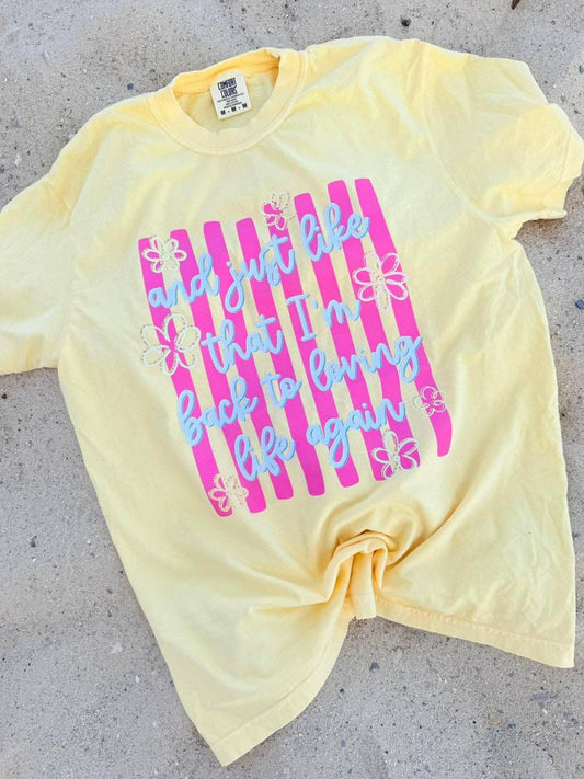 Yellow t-shirt with pink and blue text on a concrete surface