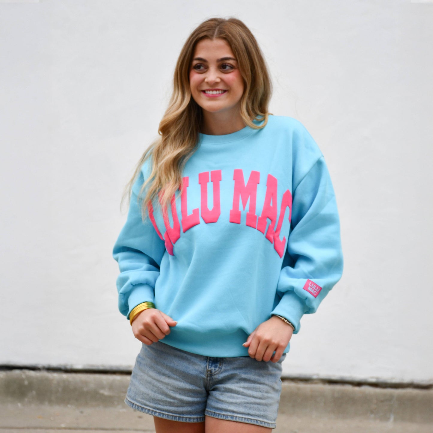 Woman wearing Lulu Mac Blue & Hot Pink Puff Sweatshirt featuring vibrant hot pink raised lettering on a bright blue fleece sweatshirt.